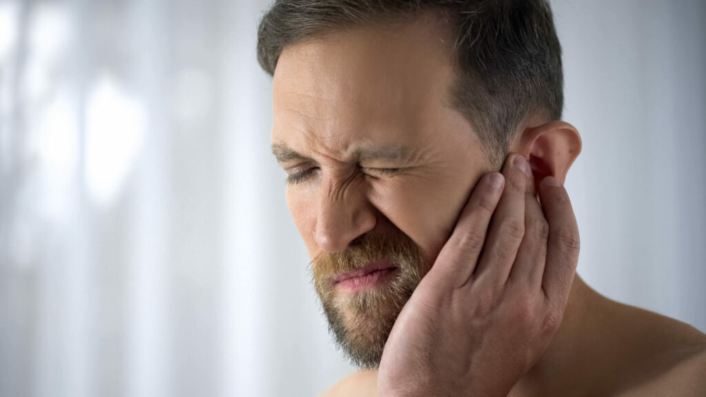 Man with beard touching jaw in pain, eyes closed and grimacing