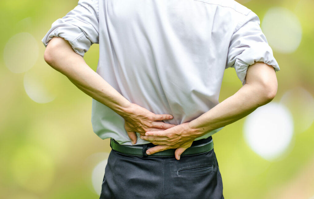 Person holding lower back with both hands, experiencing back pain or discomfort