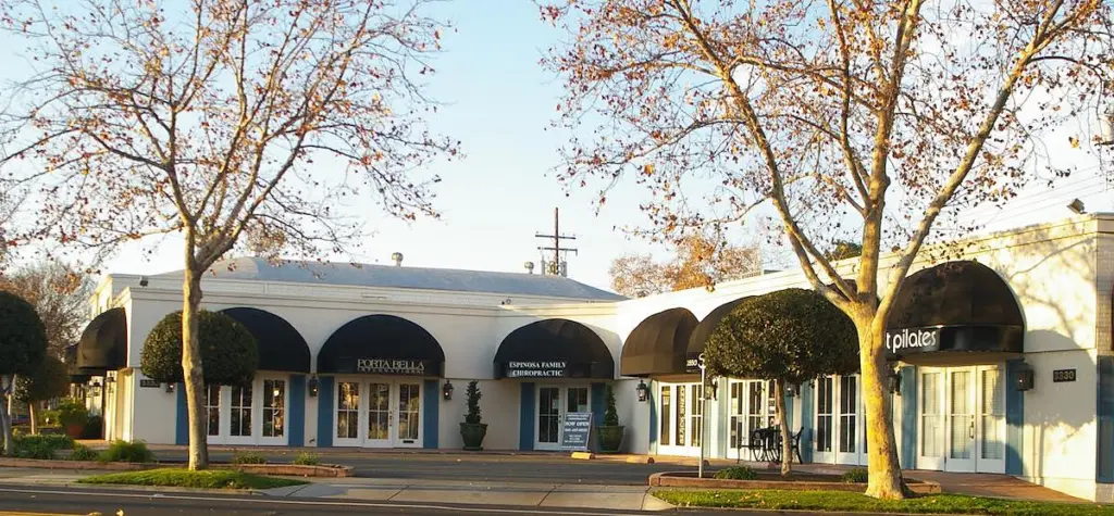 The single-storey building at 3330 Folsom Blvd: white arches and dark awnings under bare winter trees
